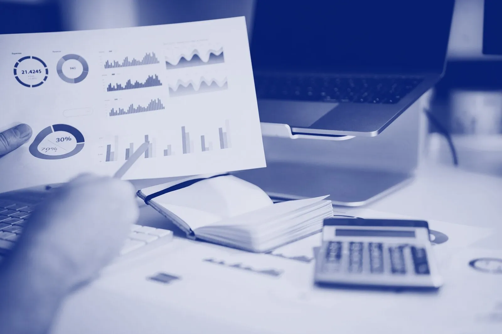 Printed charts held over a laptop, beside a notebook and calculator