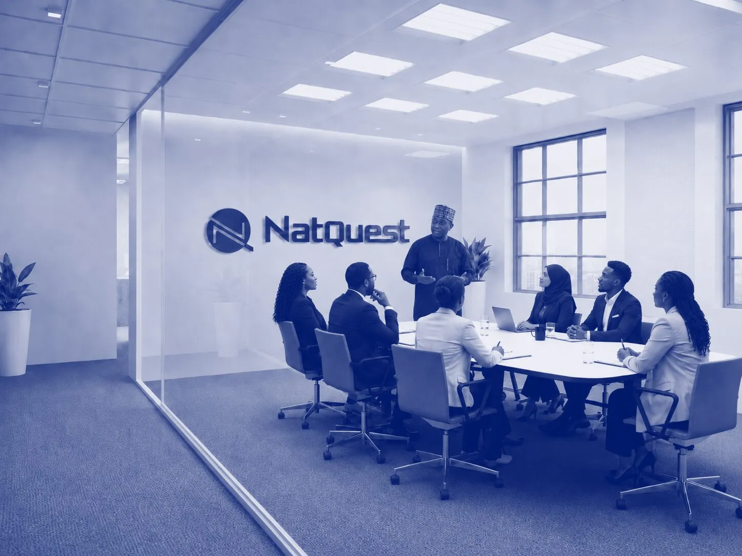A facilitator leading a session around a boardroom table, with the NatQuest logo on the wall